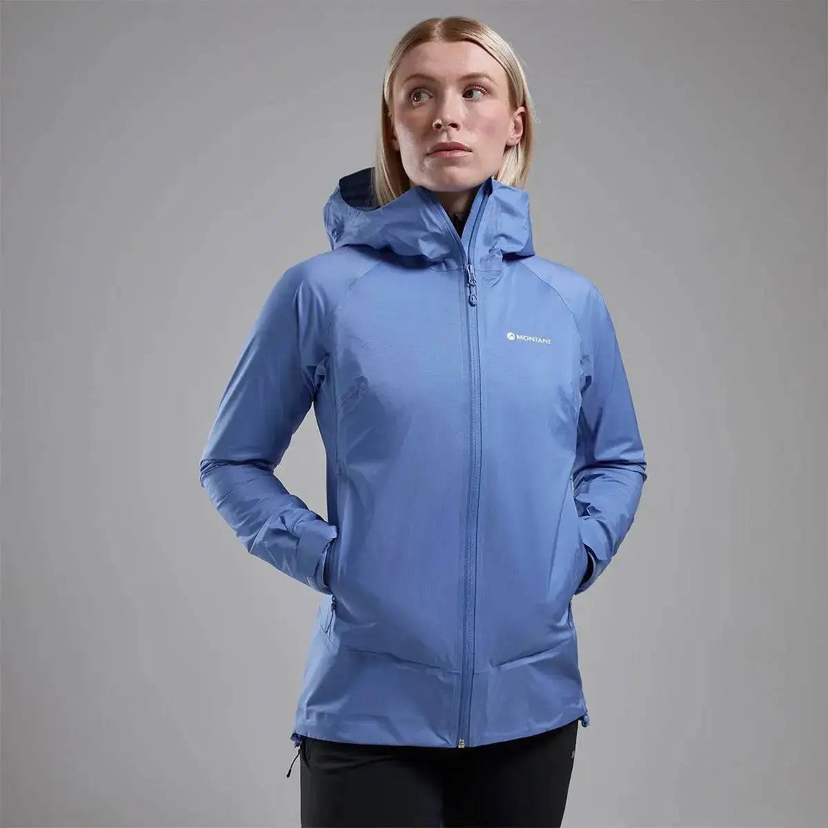Model wearing Montane Women's Cetus Lite Waterproof Jacket in light blue, featuring a fitted hood and zippered pockets for convenience. Cornflower from  John Bull Clothing 