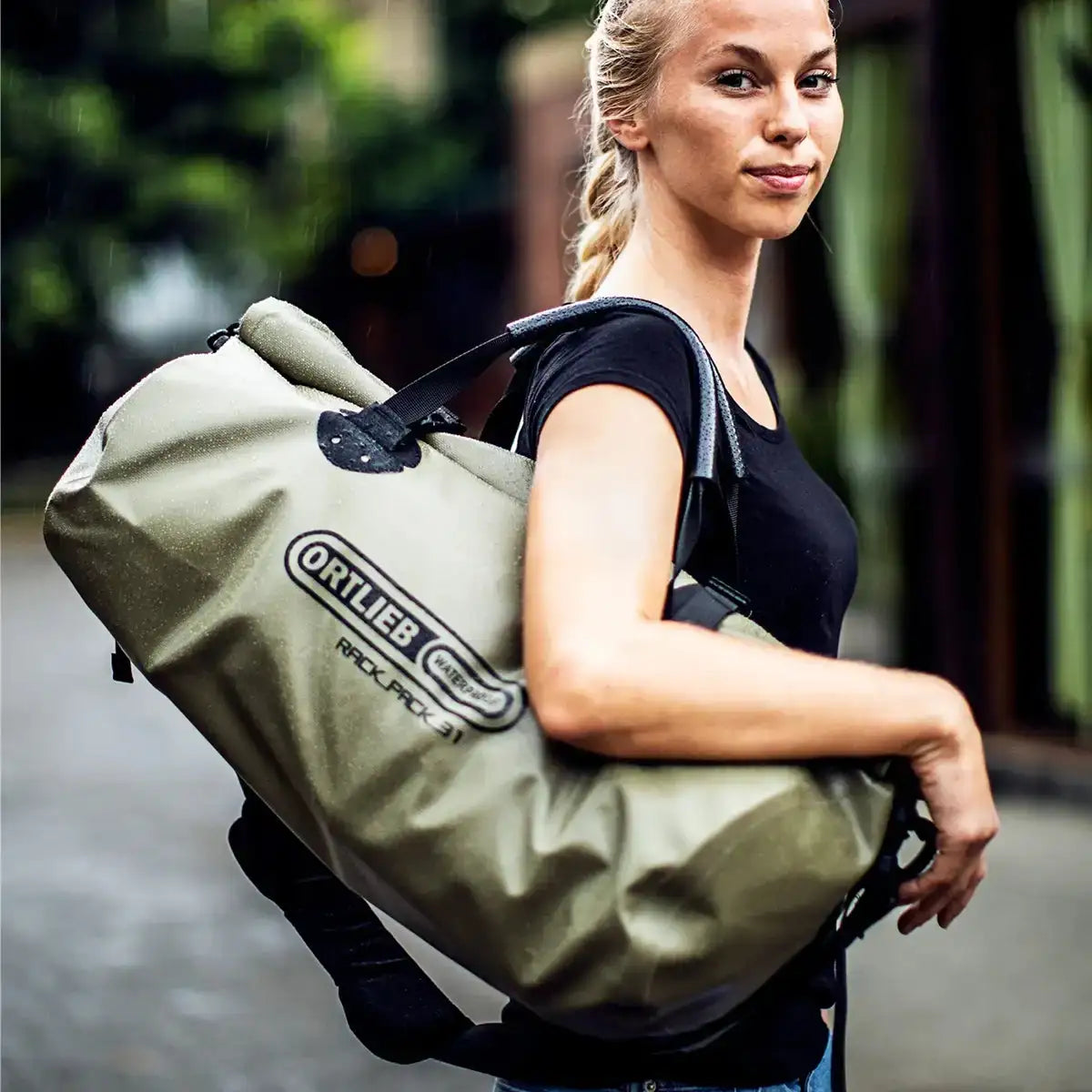 Model carrying olive Ortlieb Rack Pack 31L Waterproof Duffle Bag over shoulder, showcasing its compact size and travel-ready design.  from  John Bull Clothing 