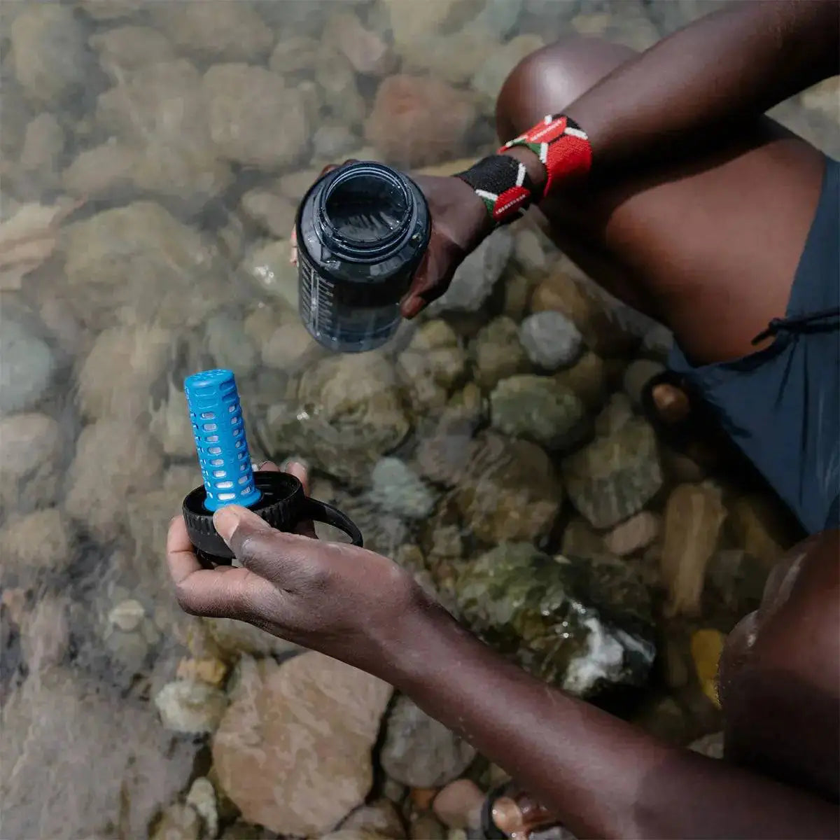 Outdoor enthusiast filling a bottle with Platypus DayCap In Water Bottle Filter from a natural water source for safe drinking.  from  John Bull Clothing 
