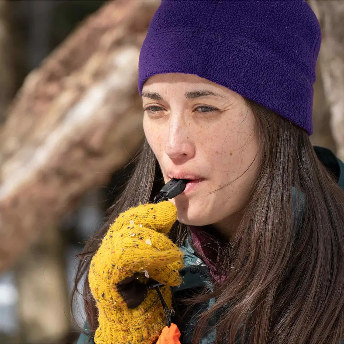 Close-up of woman using the whistle from SOL Emergency Bivvy Bag Shelter, highlighting its built-in safety feature.