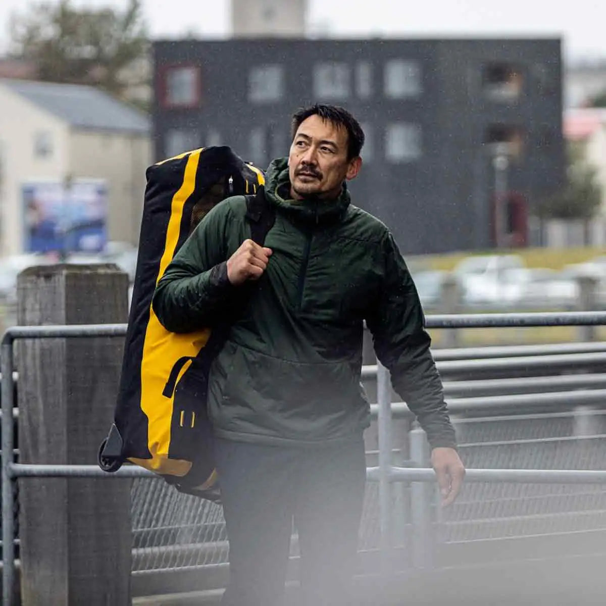 Man carrying Ortlieb Duffle RS Travel Bag 140L in black and yellow, demonstrating its portability in an outdoor setting.  from  John Bull Clothing 