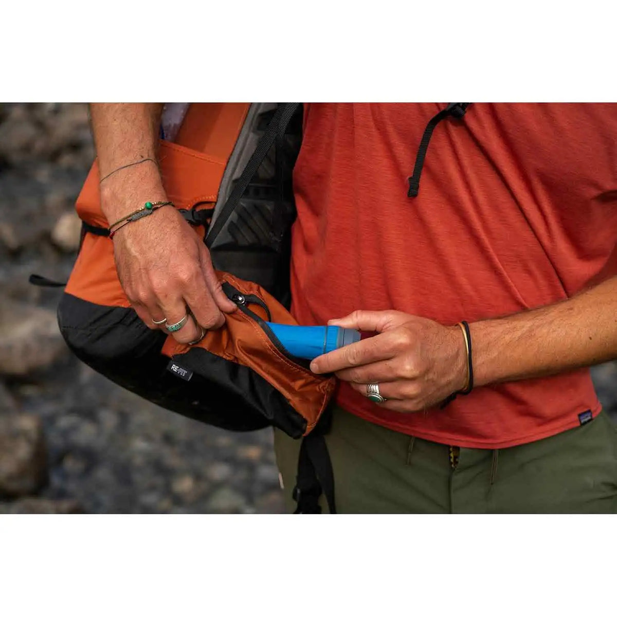A camper storing the compact Platypus Quickdraw Water Filter in a backpack pocket. Lightweight and portable for convenient outdoor hydration.  from  John Bull Clothing 